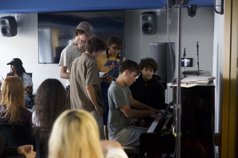 A Tisch Summer High School Recorded Music student plays an upright piano while other students stand around him at the Clive Davis Institute of Recorded Music.